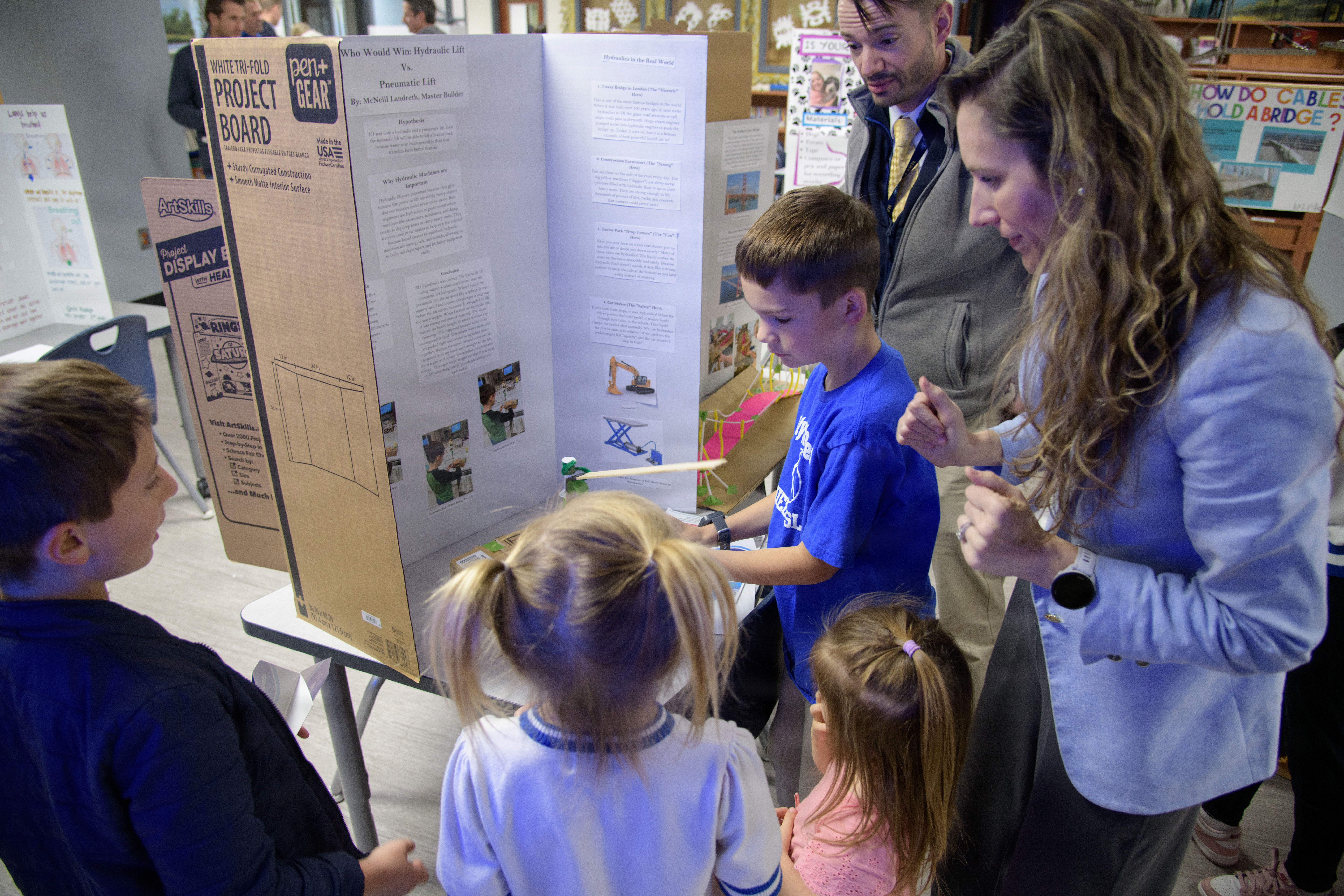 Ashlee Landreth looks on encouragingly as children interact with a school science fair project titled "Who Would Win: Hydraulic Lift Vs. Pneumatic Lift" by McNeill Landreth.