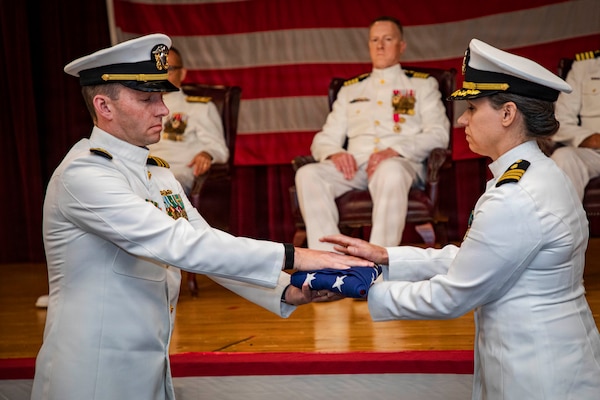Lt. Cmdr. Scott Woodson, assigned to Naval Medical Forces Atlantic (NMFL), passes an United States Flag to Cmdr. Liz Dubil, assigned to NMFL, during Capt. Chad McKenzie’s,  a native of Bellefontaine, Ohio, retirement ceremony on board Naval Support Activity (NSA) Hampton Roads - Portsmouth Annex, Portsmouth, Virginia, May 29, 2026. McKenzie served the Navy for nearly 30 years of dedicated service across 16 commands and helped advance Navy Medicine’s operational readiness and expeditionary medical capabilities in support of Fleet, Marine Corps, and joint force requirements. (U.S. Navy photo by Mass Communication Specialist 2nd Class Levi Decker)