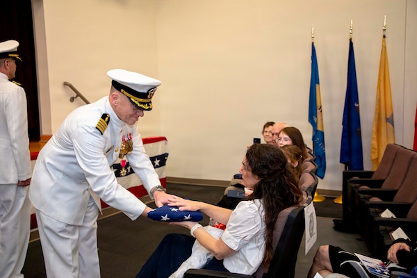 Naval Medical Forces Atlantic Deputy Commander, Capt. Chad McKenzie,  a native of Bellefontaine, Ohio, presents an United States flag to his wife during his retirement ceremony on board Naval Support Activity (NSA) Hampton Roads - Portsmouth Annex, Portsmouth, Virginia, May 29, 2026. McKenzie served the Navy for nearly 30 years of dedicated service across 16 commands and helped advance Navy Medicine’s operational readiness and expeditionary medical capabilities in support of Fleet, Marine Corps, and joint force requirements. (U.S. Navy photo by Mass Communication Specialist 2nd Class Levi Decker)