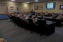 USAF Airman stands briefing USAF Airmen and civilians sitting at a conference table