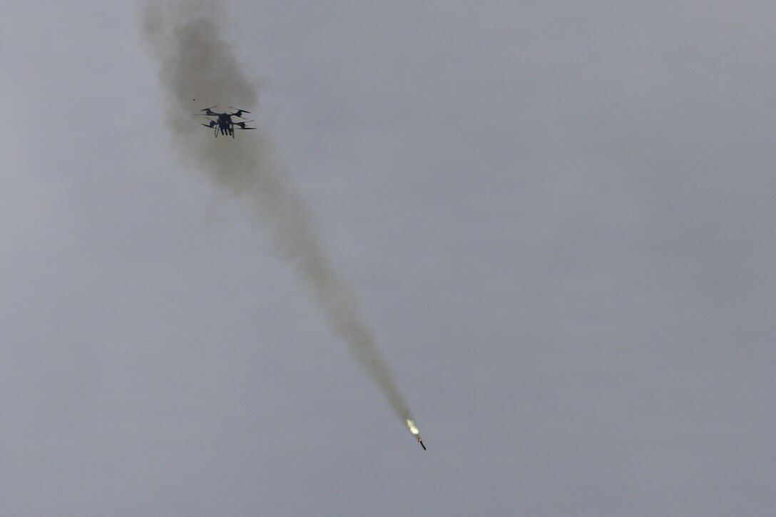 A projectile leaves a trail of smoke as it shoots from a drone flying in gray sky.