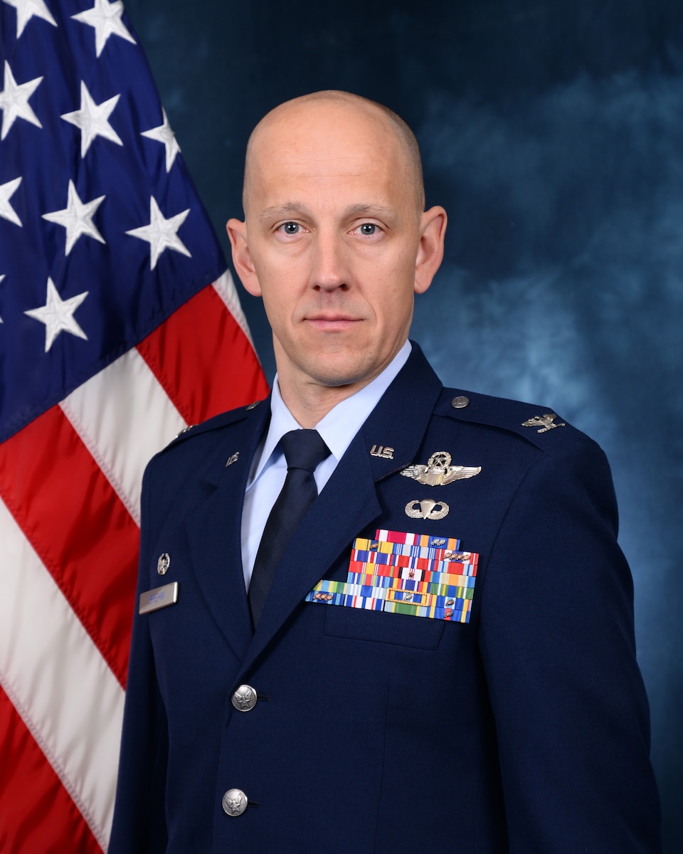 Male Air Force Officer in dress blues standing in front of an American flag