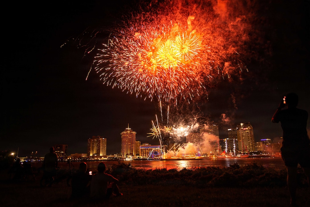Ships next to a city's shoreline fire fireworks into the dark sky, creating a colorful display.