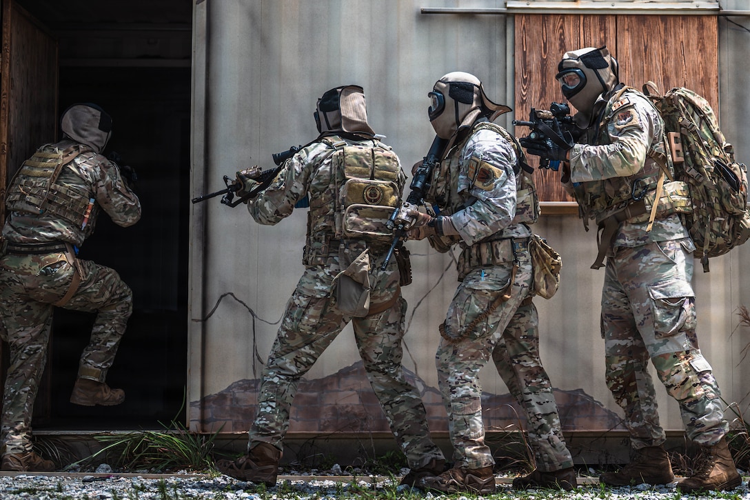 Five airmen in tactical and protective gear prepare to enter a gray container.