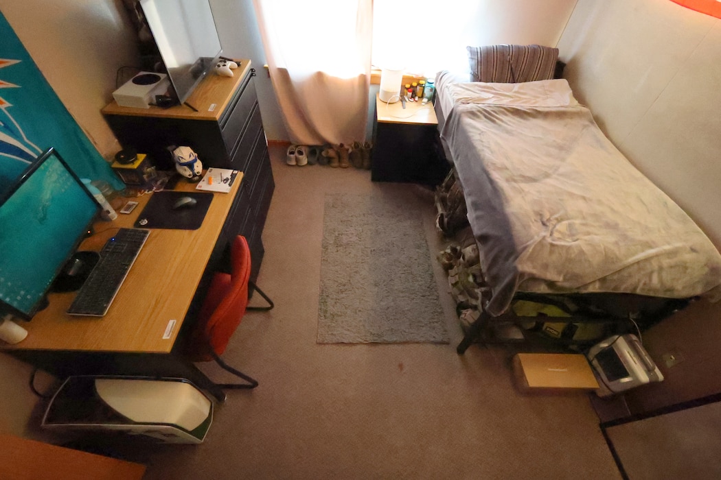 Image of a bed, a chest of drawers and a desk in a barracks bedroom.