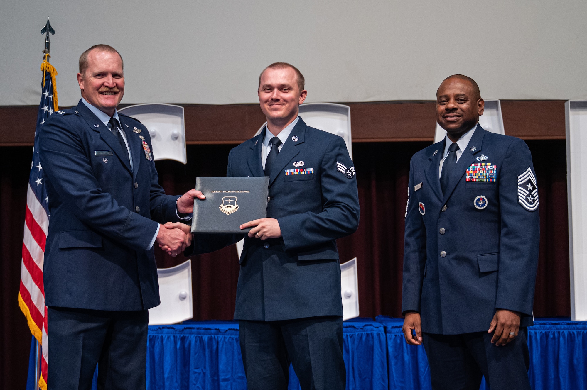 U.S. Air Force Senior Airman Noah Hartkopf, 26th Network Operations Squadron, receives his diploma from Col. Adam Rudolphi, left, 42d Air Base Wing deputy commander and Chief Master Sgt. Demetrius Booth, 42d ABW command chief, during a Community College of the Air Force graduation at Gunter Annex, Alabama, May 28, 2026.
