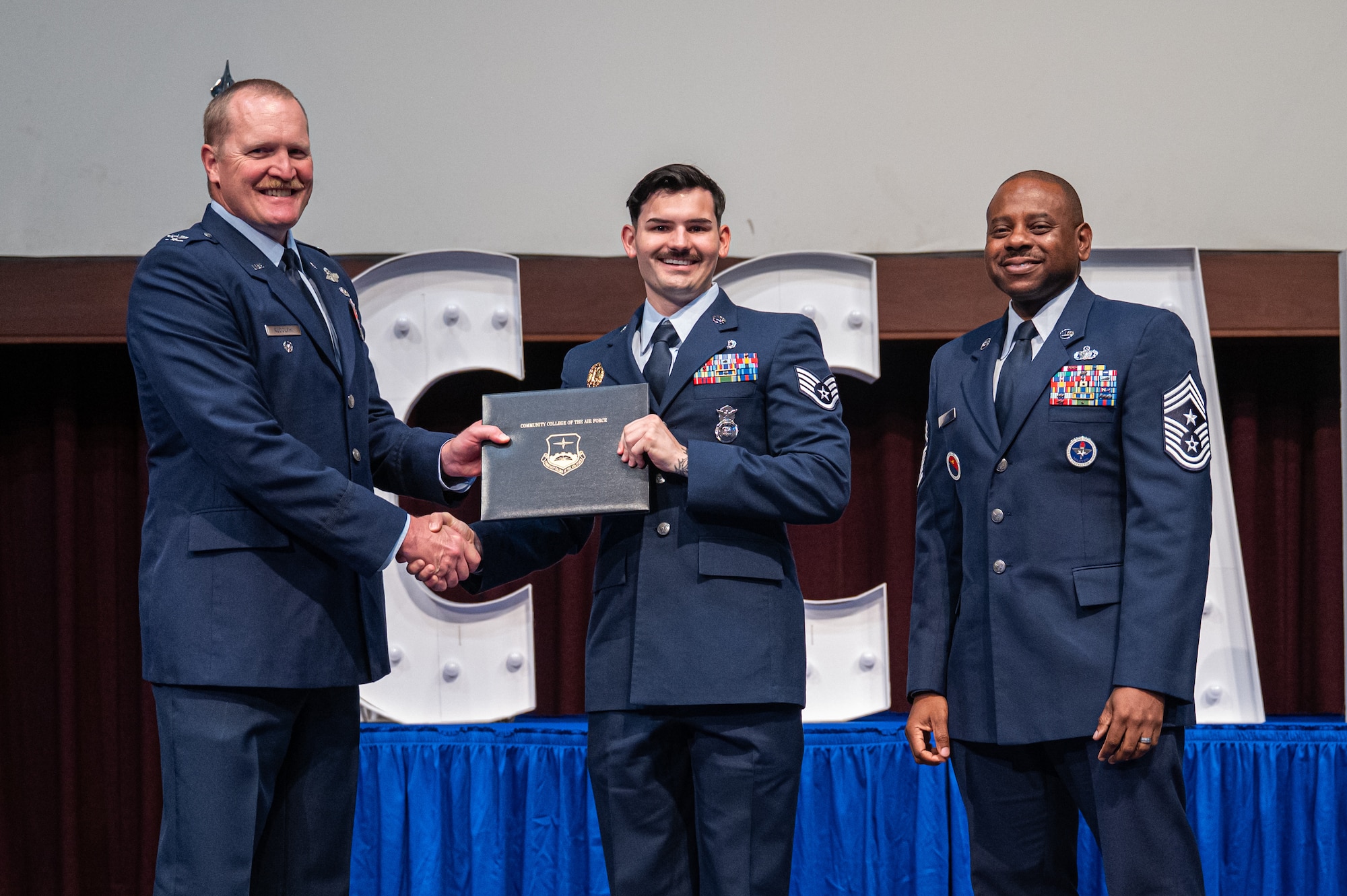 U.S. Air Force Staff Sgt. Vincent Gorrusso, 42d Security Forces Squadron, receives his diploma from Col. Adam Rudolphi, left, 42d Air Base Wing deputy commander and Chief Master Sgt. Demetrius Booth, 42d ABW command chief, during a Community College of the Air Force graduation at Gunter Annex, Alabama, May 28, 2026.