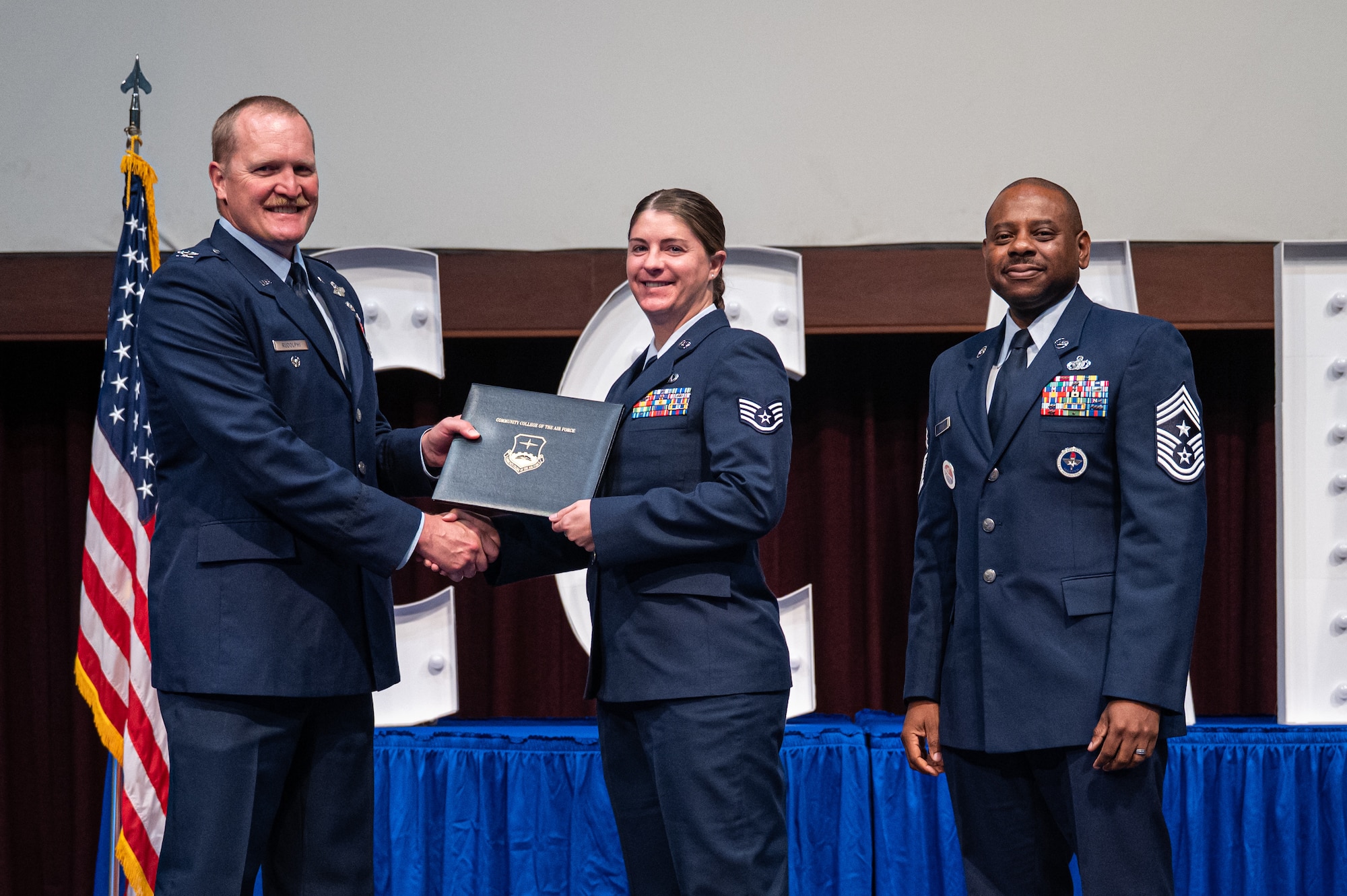 U.S. Air Force Staff Sgt. Samantha Shaffer, Community Colle of the Air Force, receives her diploma from Col. Adam Rudolphi, left, 42d Air Base Wing deputy commander and Chief Master Sgt. Demetrius Booth, 42 ABW command chief, during a Community College of the Air Force graduation at Gunter Annex, Alabama, May 28, 2026.