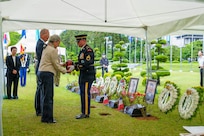Staff at the United Nations Memorial Cemetery Korea present a flag‑draped urn containing the remains of French Korean War veteran Jacques Grisolet to his family during an interment ceremony in Busan, South Korea, on May 27, 2026. Family members stand solemnly as cemetery officials complete the handoff, honoring both Grisolet and fellow veteran André Datcharry. The scene takes place outdoors among manicured grounds and memorial markers, reflecting the ceremony’s recognition of France’s sacrifice during the Korean War and its ongoing support to the United Nations Command.