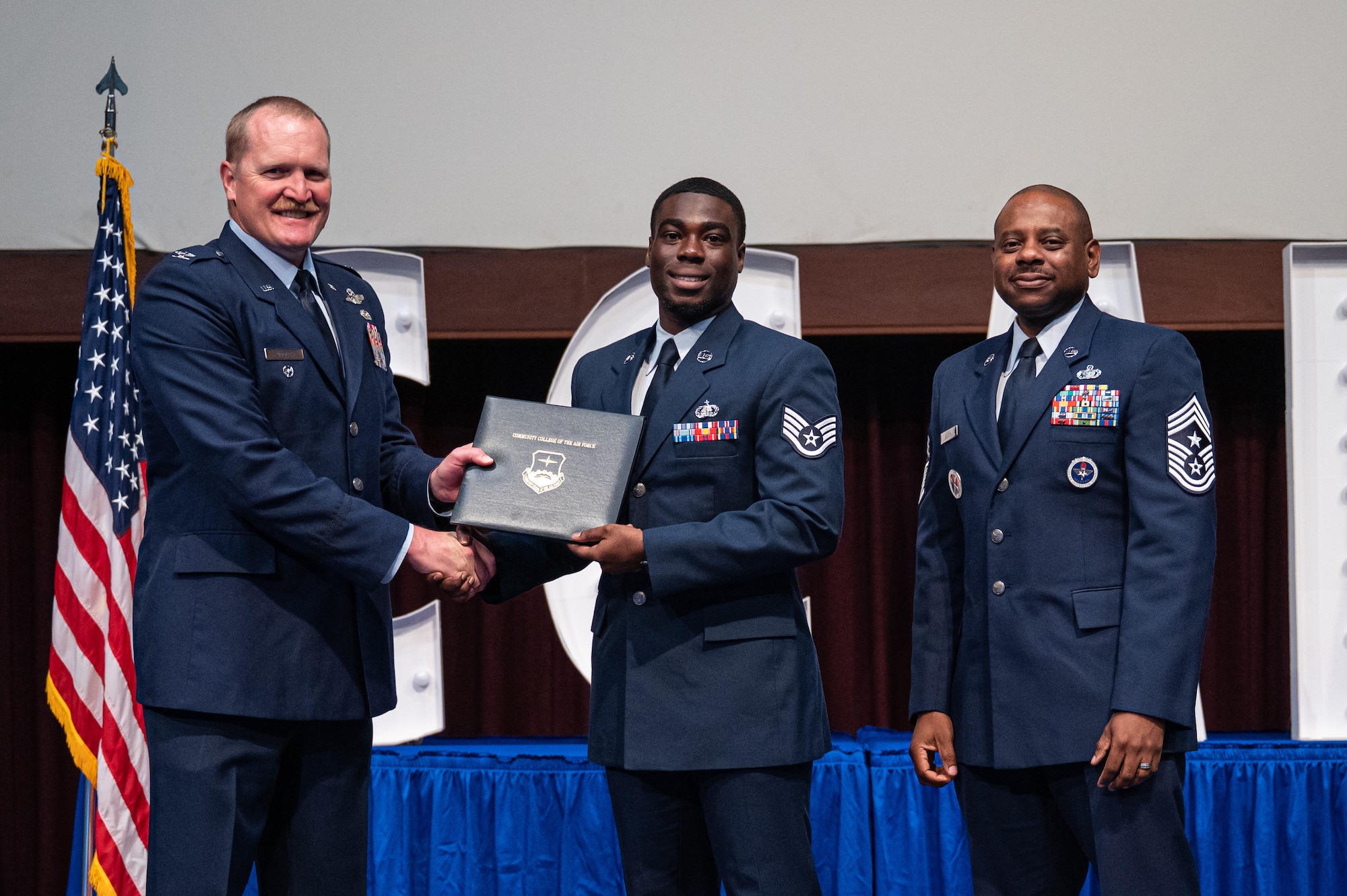 U.S. Air Force Staff Sgt. Yves Jacquet, Air Education and Training Command AFROTC, receives his diploma from Col. Adam Rudolphi, left, 42d Air Base Wing deputy commander and Chief Master Sgt. Demetrius Booth, 42d ABW command chief, during a Community College of the Air Force graduation at Gunter Annex, Alabama, May 28, 2026.