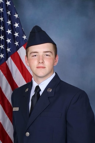 An Airman poses for a photo in front of a flag.