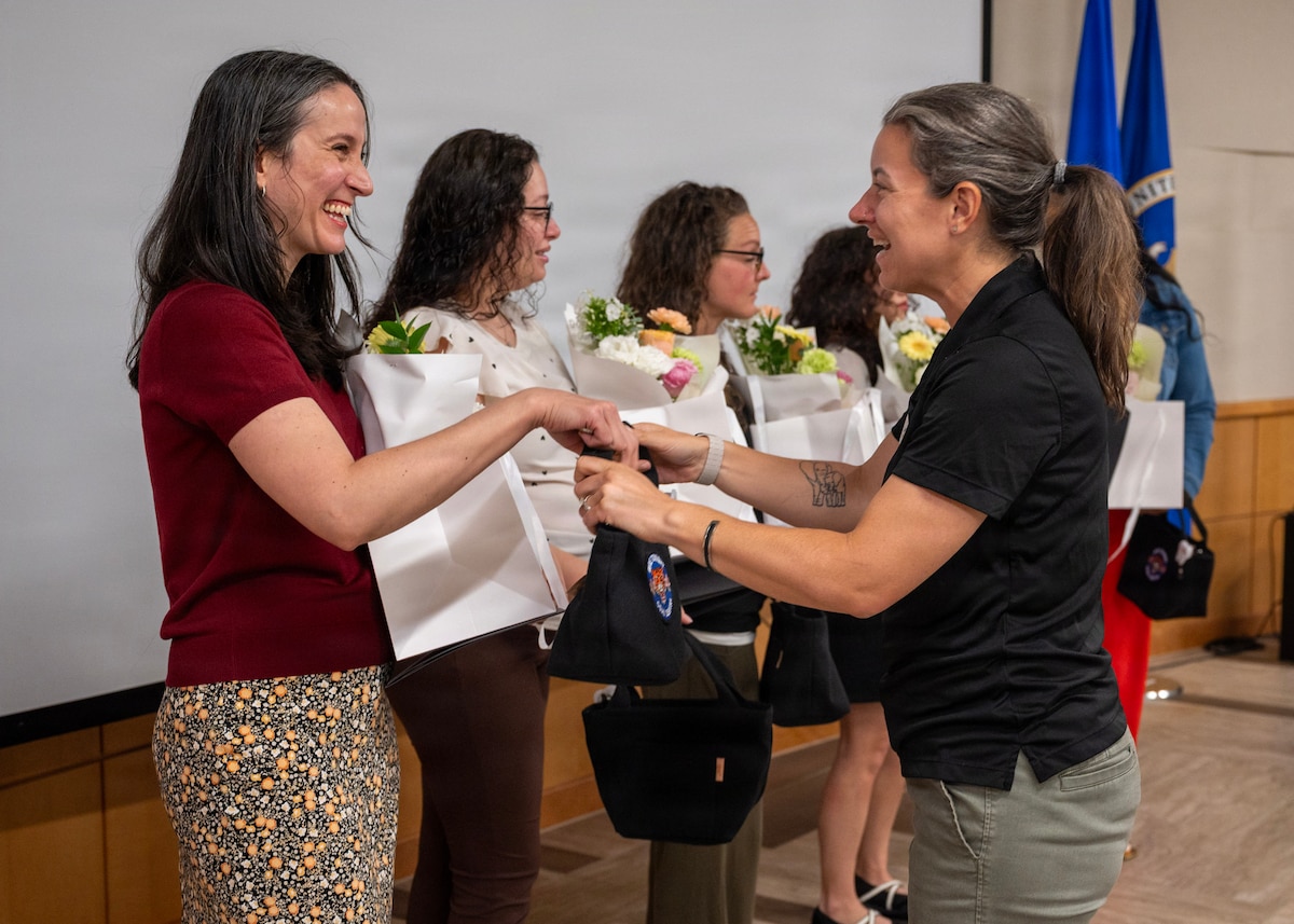 Woman wearing a red shirt and floral bottoms is given a bouquet of flowers