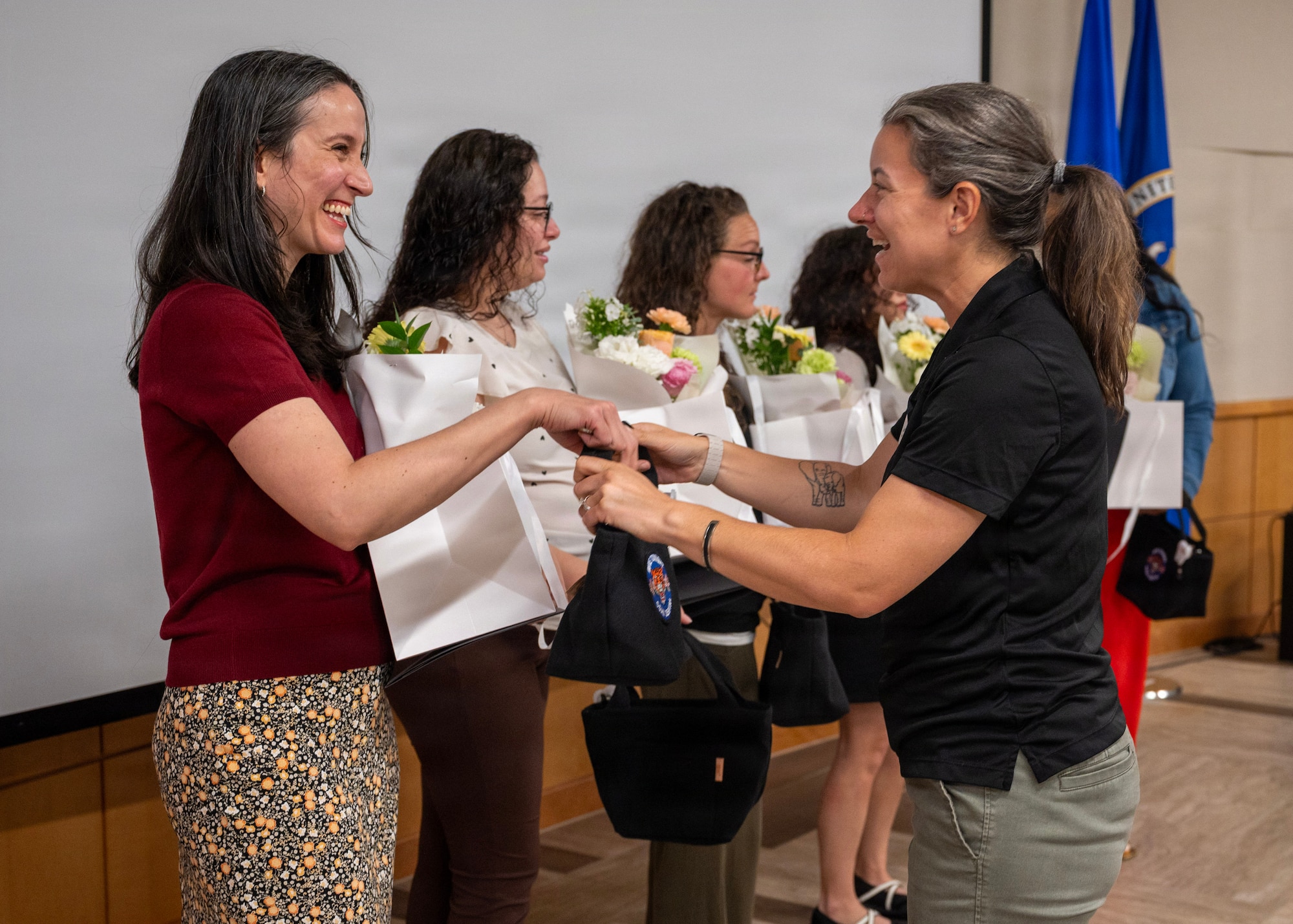 Woman wearing a red shirt and floral bottoms is given a bouquet of flowers