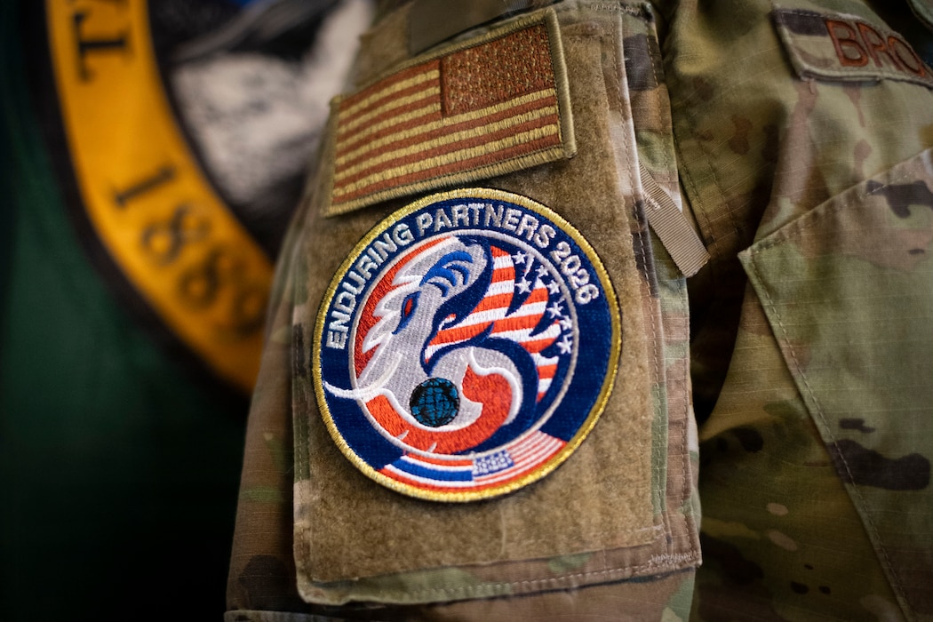 A close up on a sleeve of a U.S. Airman. On the sleeve are two patches. The upper, an olive drab U.S. flag. Below that is a circular patch in the colors or the U.S. and Thai flag: red white and blue, with the words "Enduring Partners 2026" in an arch across the top.