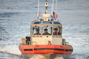 Three men wearing life jackets sail in a small boat in the ocean; the Philippine and American flags are flying from the top of the boat.