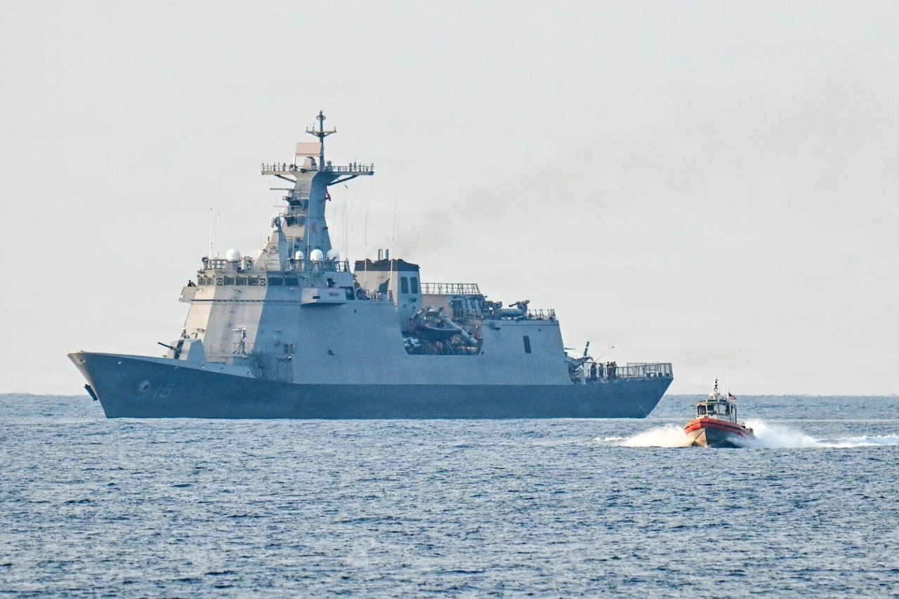 A small boat sails away from a large ship in the ocean.