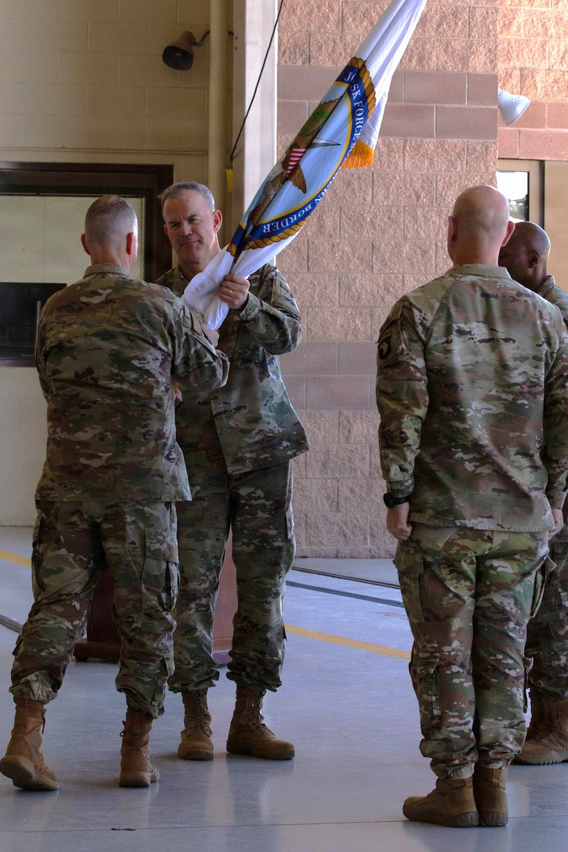Two men in camouflage military uniforms hold a white flag as two other men in similar attire stand at attention next to them in an aircraft hangar.