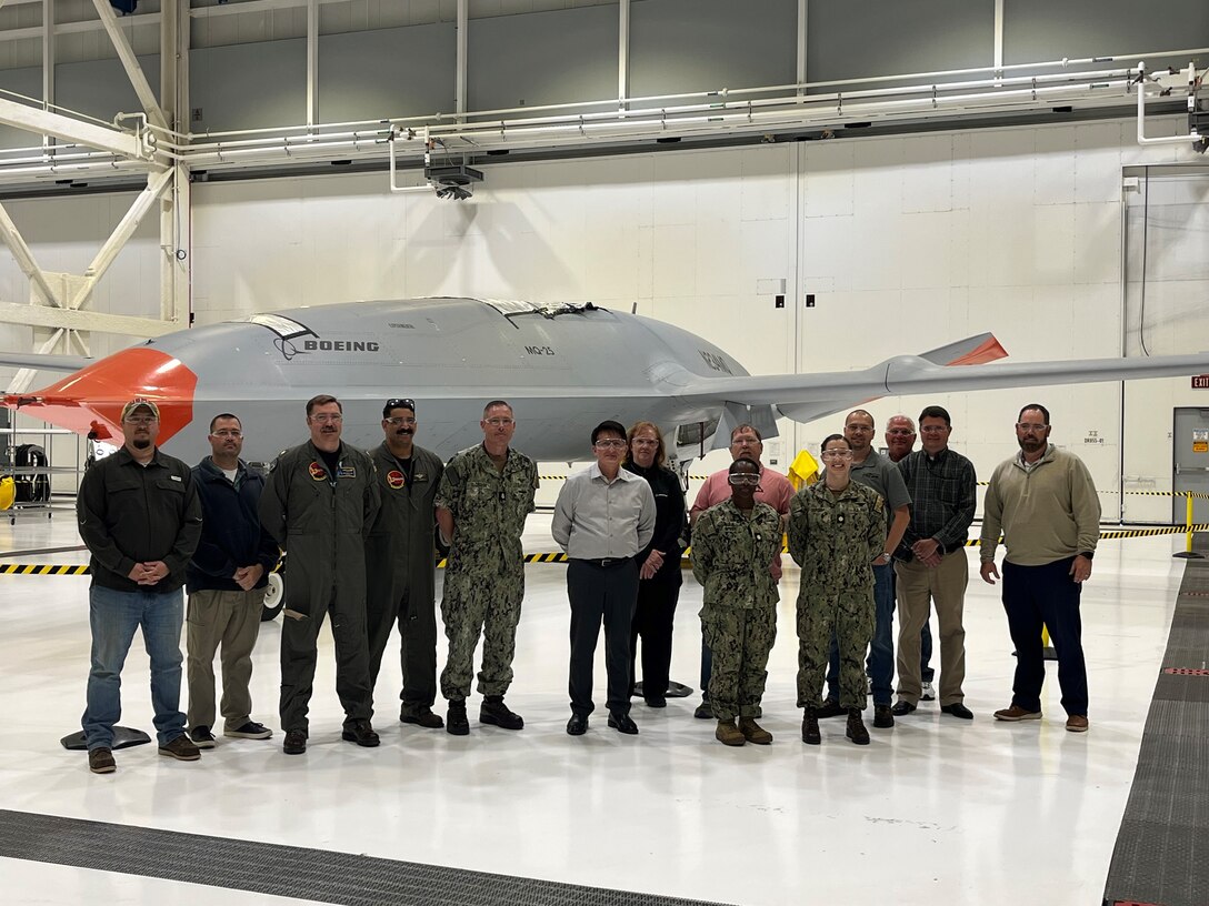 A group of military and civilian personnel stand in front of an aircraft