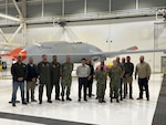 A group of military and civilian personnel stand in front of an aircraft