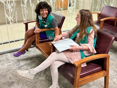 Two Girl Scouts sit in a waiting room talking about a book.