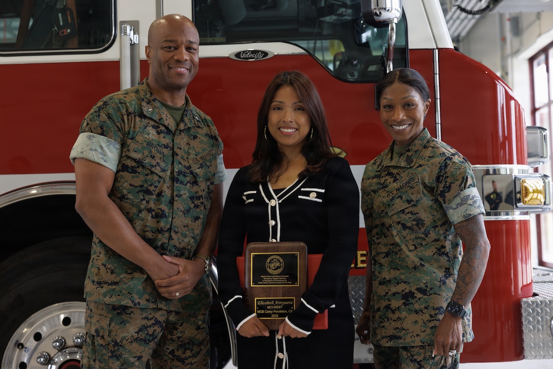 A person holds an award between two people, smiling for a photo.