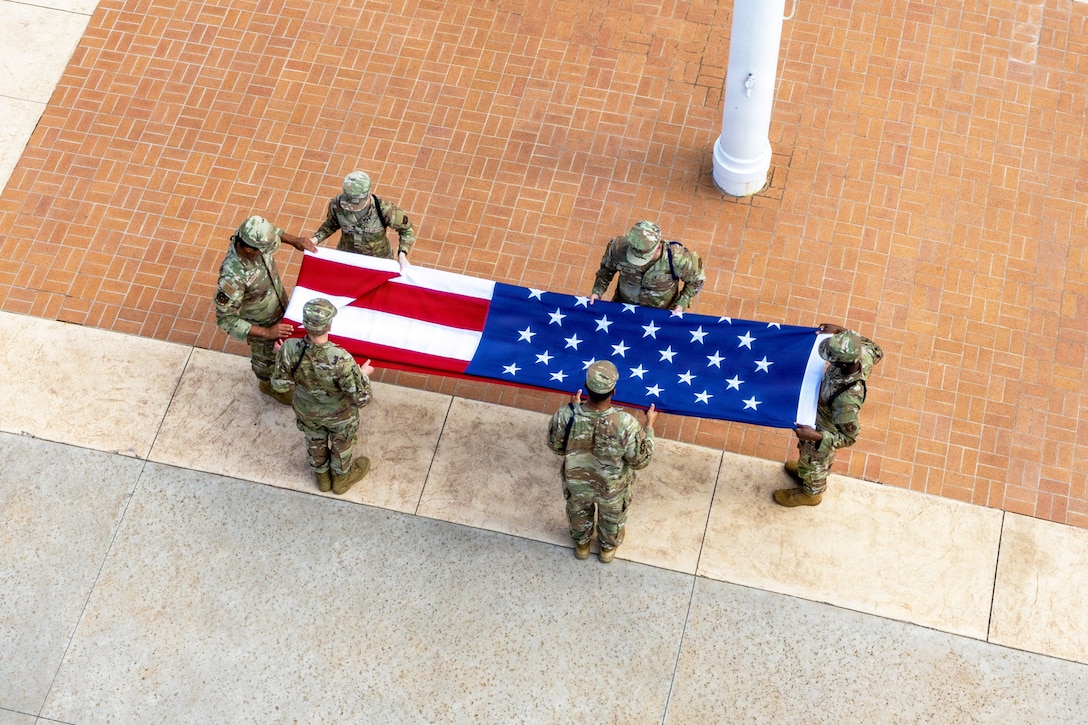 Six airmen fold a large American flag as seen from above.