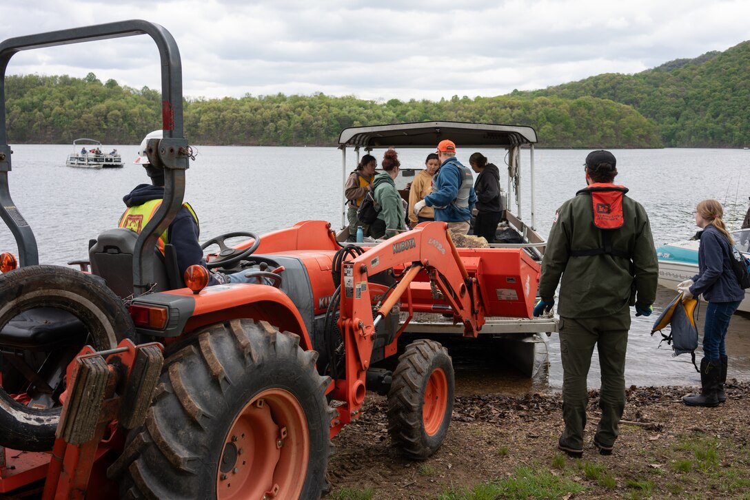 A red tractor with front lift sitting on a lakeshore removes trash from a boat.