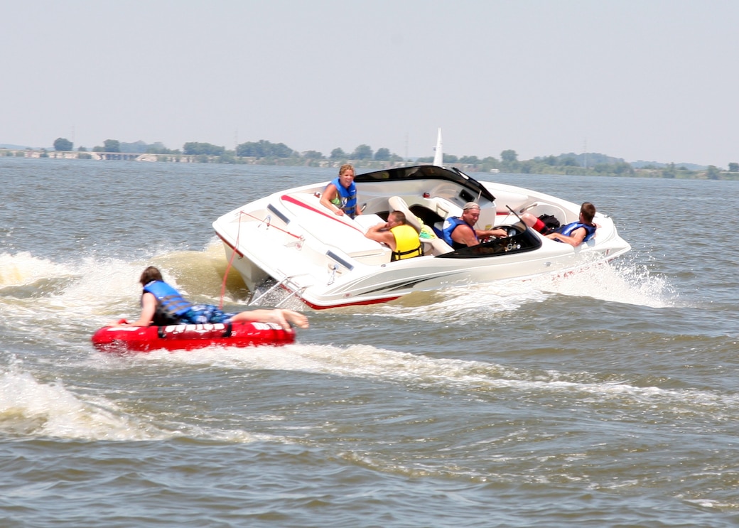 A small motorized boat with four passengers pulls another passenger on a tube.