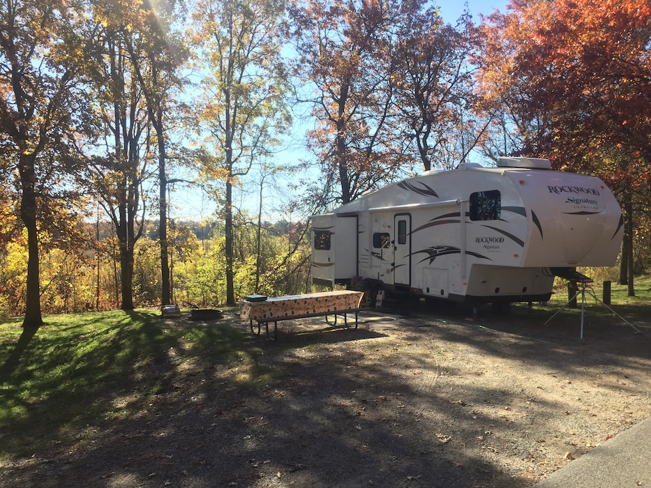 An RV parked next to a picnic table at a bright, wooded campsite.