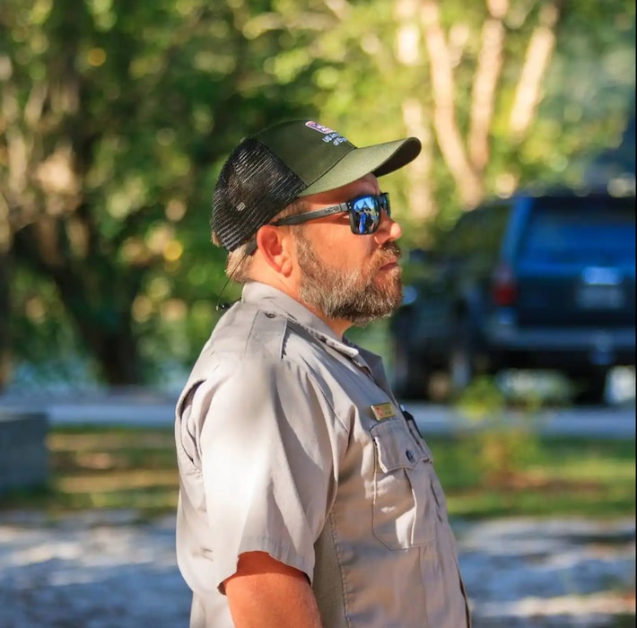 A man wearing sunglasses, hat, and a ranger outfit looks ahead.