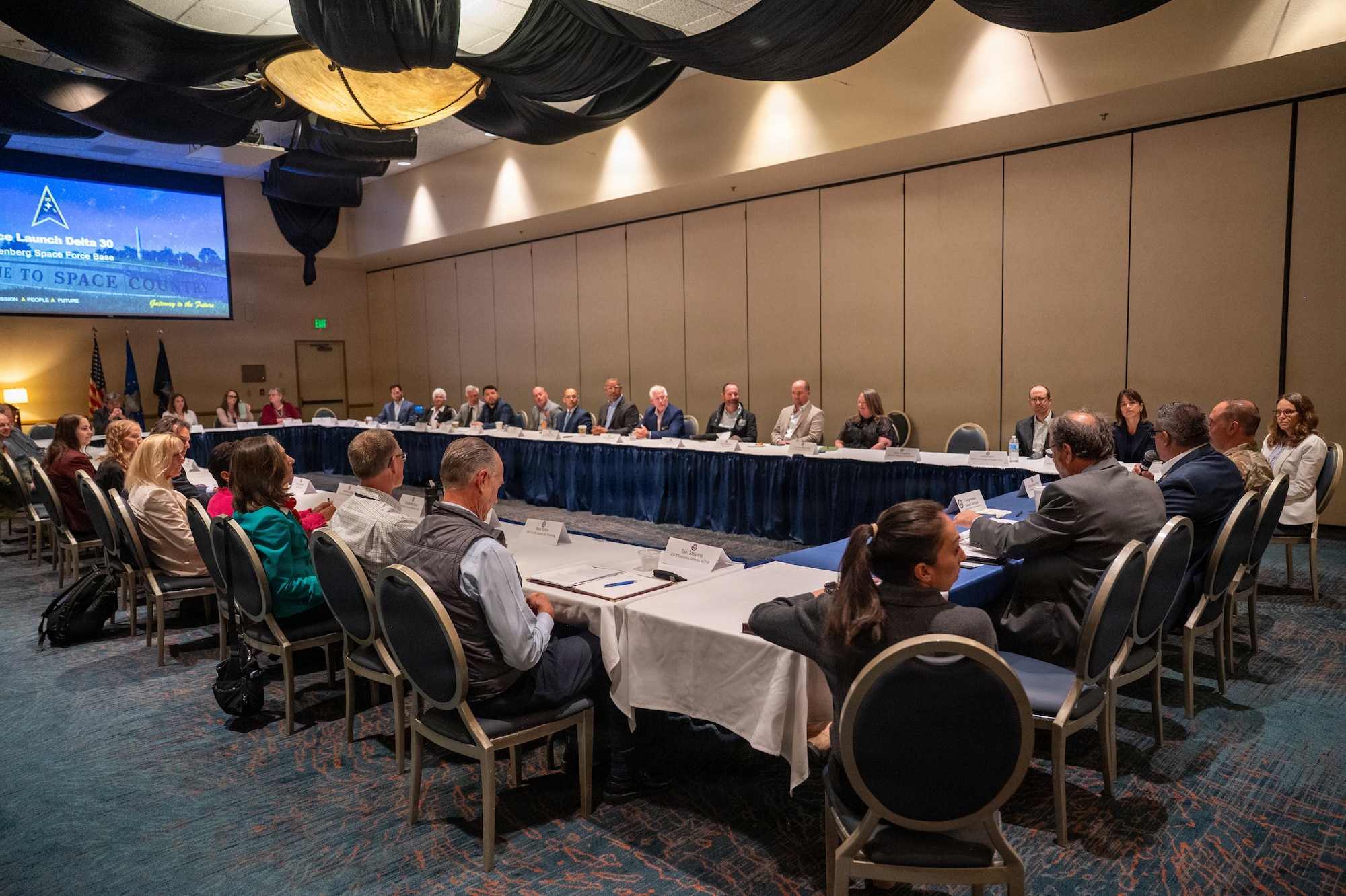 A group of people sit at a roundtable and listen to discussion.