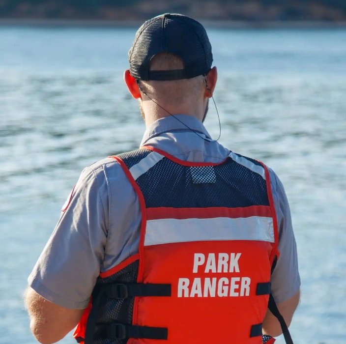 A man wearing a ranger shirt and USACE hat from behind, wearing a life jacket that reads Park Ranger.