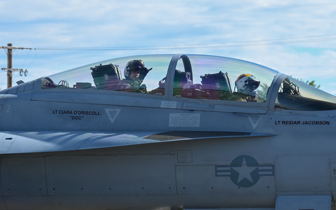 A U.S. Navy co-pilot for the EA-18G Growler, assigned to the Electronic Attack Squadron (VAQ) 138, signals their unit hand sign on the flightline at Eielson Air Force Base, Alaska, June 1, 2026.