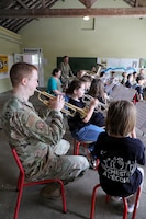 U.S. Airmen with the Five Star Brass, U.S. Air Forces in Europe, Air Forces Africa Band , play their instruments alongside school children during a musical exchange at the Ecole Primaire Les Hauts Champs in Carentan-les-Marais, France, June 2, 2026. The exchange highlights our shared values of free cultural expression while building a connection between U.S. service members and a new generation in Normandy. From June 2-7, 2026, more than 600 U.S. Soldiers, Sailors, Marines, Guardians and Airmen from roughly 17 units historically linked to D-Day made up Joint Task Force 82 and participated in over 90 commemorative events throughout the Normandy Region. (U.S. Army National Guard photo by 1st Sgt. HollyAnn Nicom)
