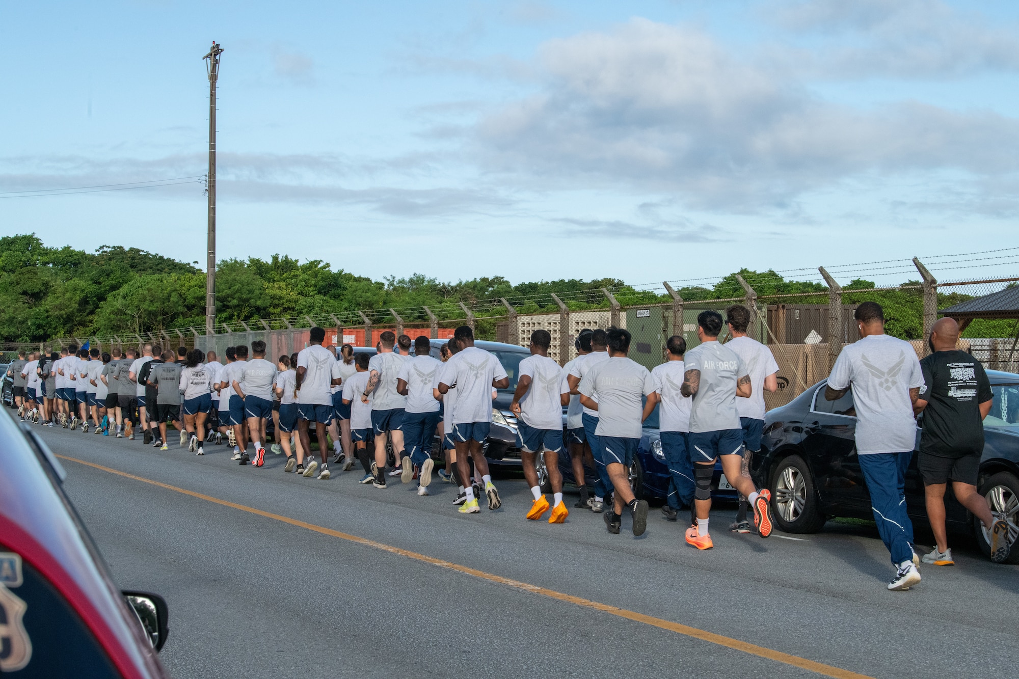 A large squadron of Airmen run on the sidewalk