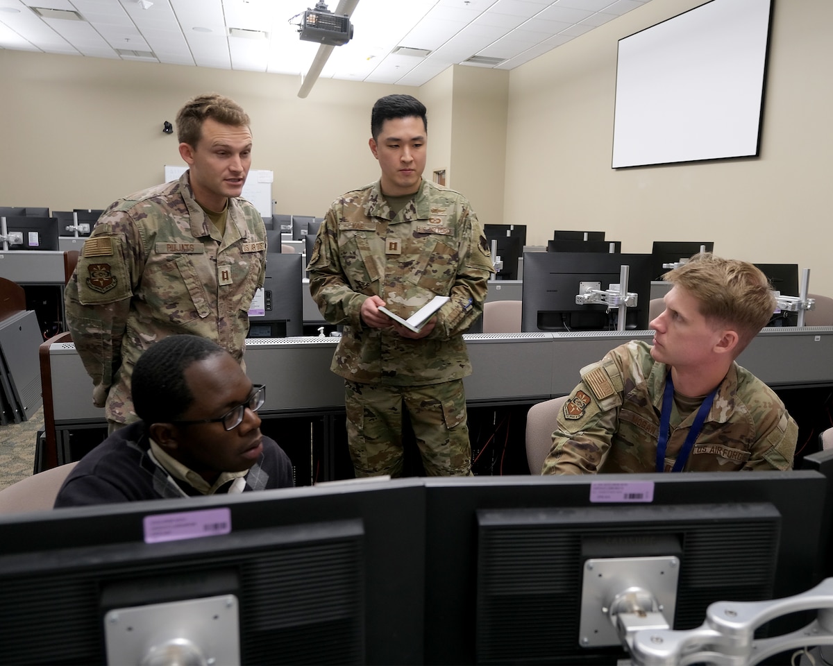 uniformed U.S. military and a civilian talking in a room full of computer screens
