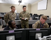 uniformed U.S. military and a civilian talking in a room full of computer screens