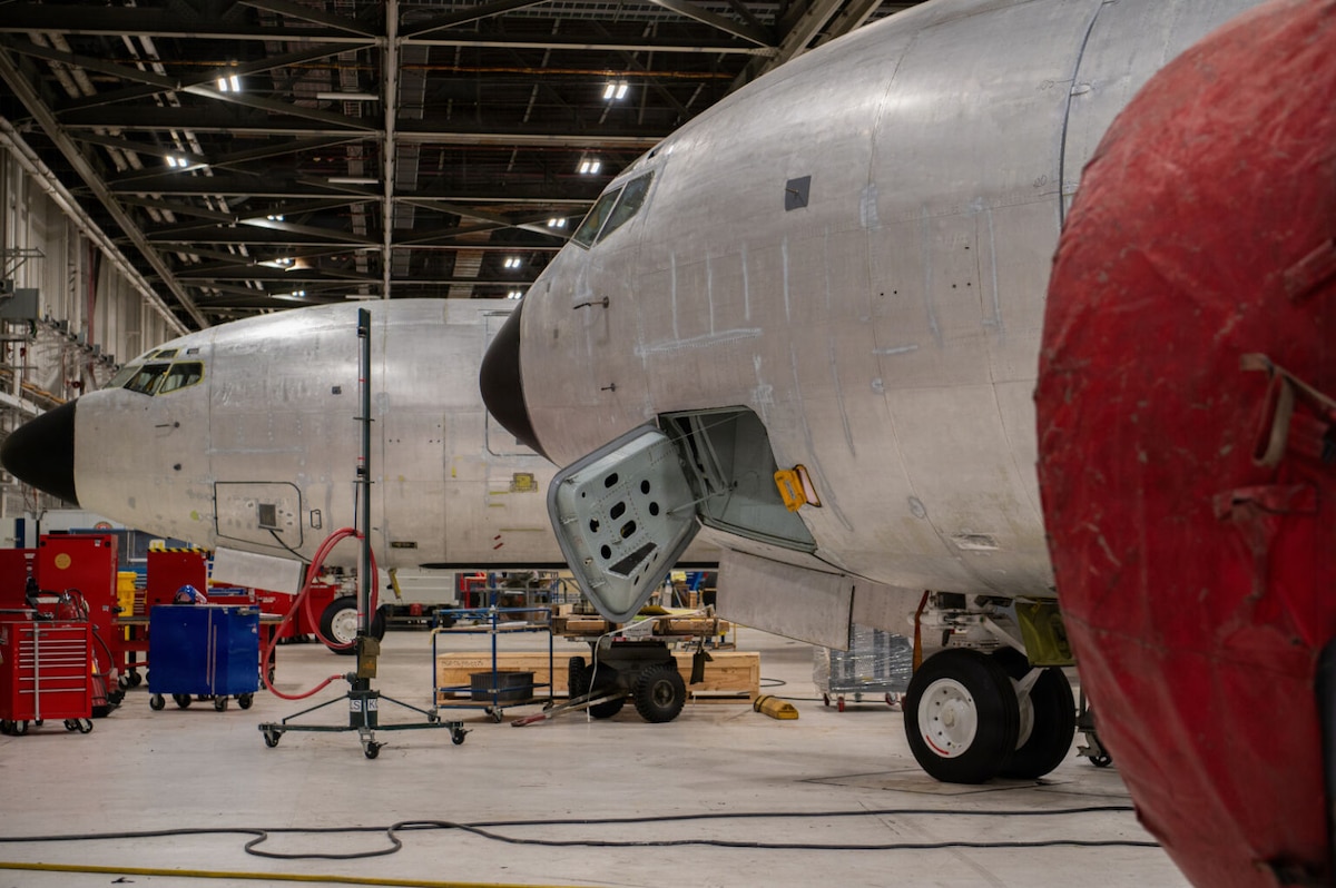 Two aircraft are parked in a maintenance hangar, one of the aircraft has its access door open.