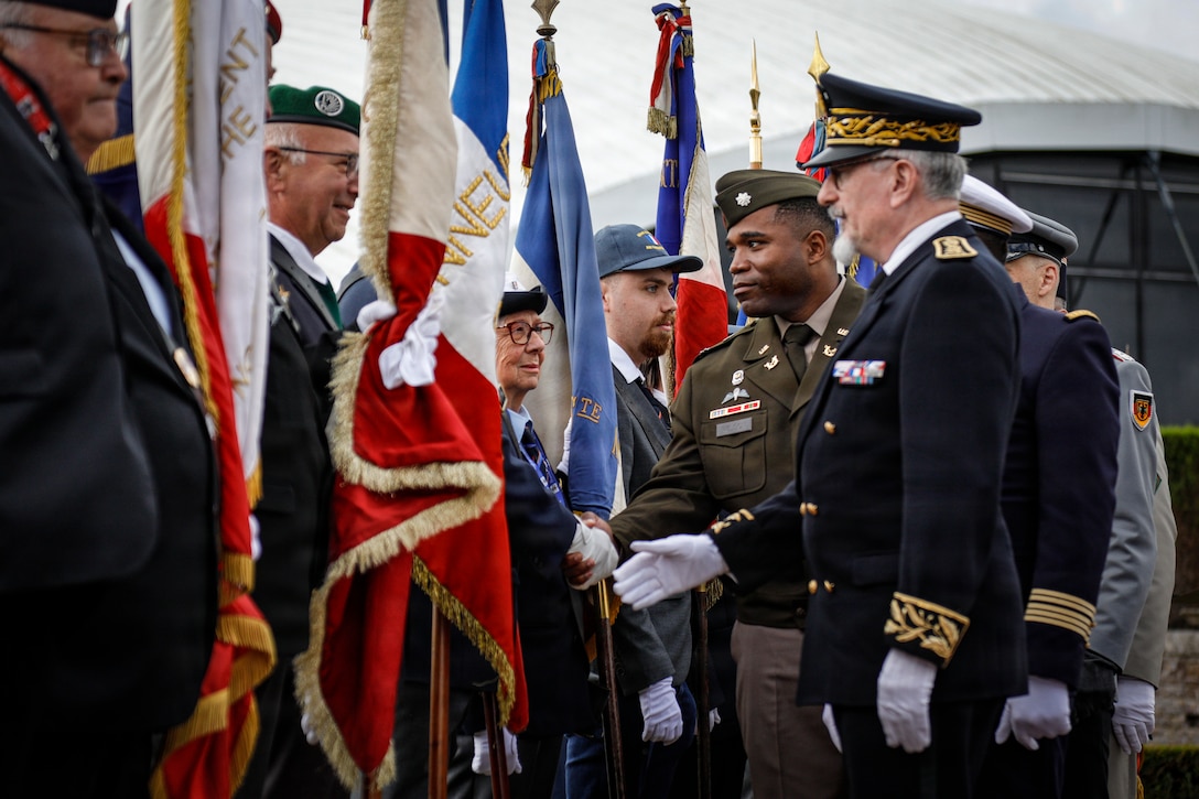 U.S. Army Lt. Col. Earl Wilson, deputy staff judge advocate, Headquarters and Headquarters Battalion, 82nd Airborne Division, shakes the hands of the French regimental flag bearers at the Three Cemeteries Monument, Sainte-Mère-Église, France, June 2, 2026. The Three Cemeteries Monument honors the 14,000 U.S. troops, particularly from the 82nd Airborne Division, who fell during the battle to liberate Normandy, France. (U.S. Army photo by Staff Sgt. Catessa Palone)