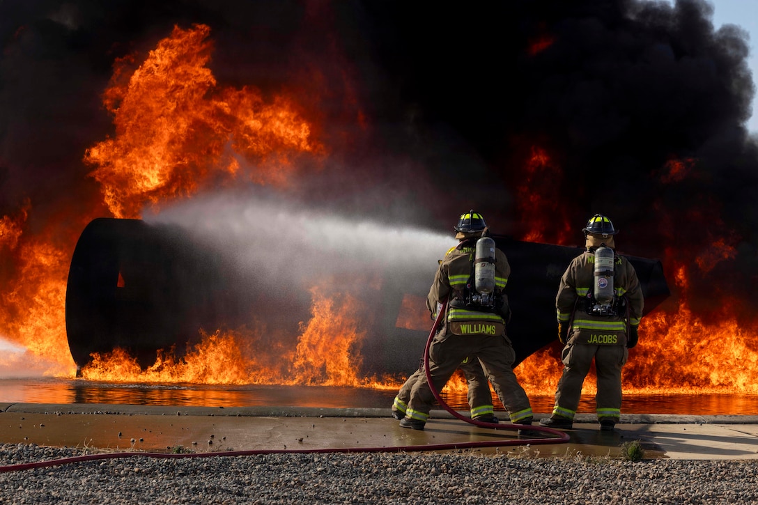 Three firefighters use a hose to put out a large fire.