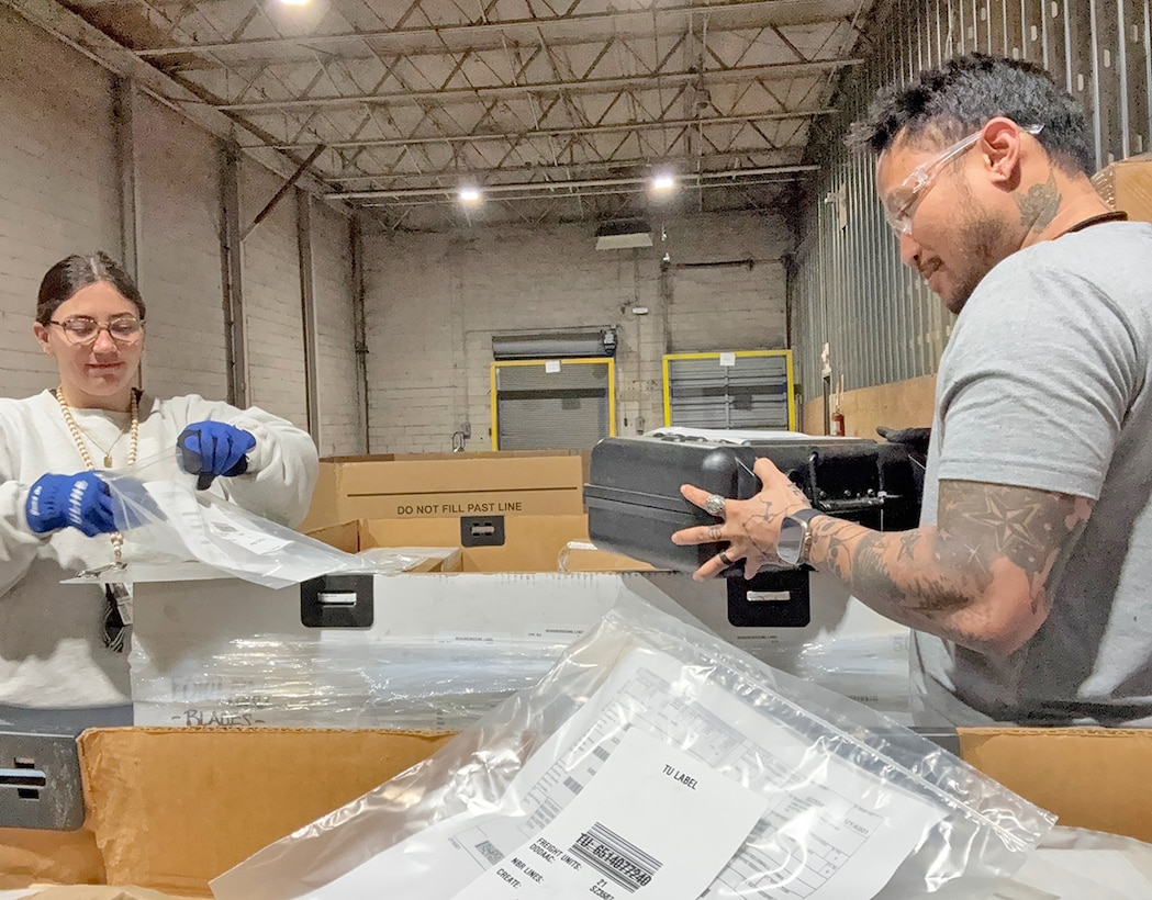 Two people examine electronics in a warehouse.