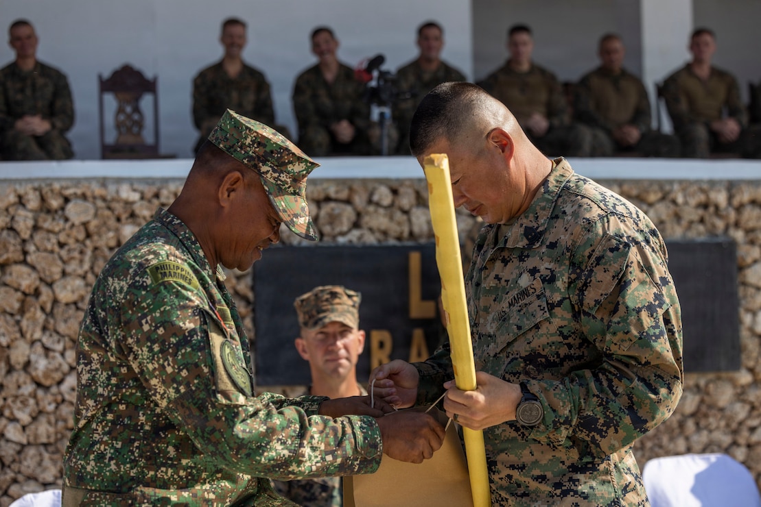 From left, Philippine Marine Corps Sgt. Maj. Ariel Mesa, the sergeant major of 4th Marine Brigade, gives a token of appreciation  to U.S. Marine Corps 1st Sgt. Christopher Lee, a native of Hawaii and the outgoing command senior enlisted leader assigned to 3rd Littoral Combat Team, 3rd Marine Littoral Regiment, 3rd Marine Division, for a relief and appointment ceremony at Camp Cape Bojeador, Philippines, May 17, 2026. The passing of the sword during the ceremony symbolized the transfer of authority and responsibility from 1st Sgt. Christopher Lee, the outgoing command senior enlisted leader, to Sgt. Maj. Christian Hutson, the incoming command senior enlisted leader of 3rd LCT. (U.S. Marine Corps photo by Sgt. Iyer Ramakrishna)