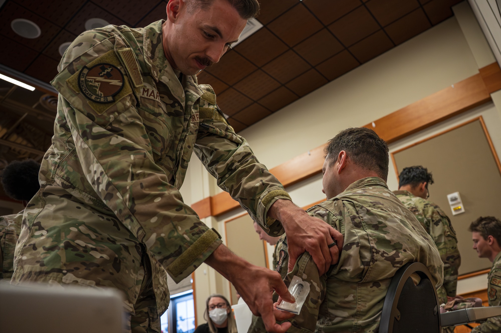 A U.S. Air Force medical professional administers a simulated vaccination to a man during a training exercise.