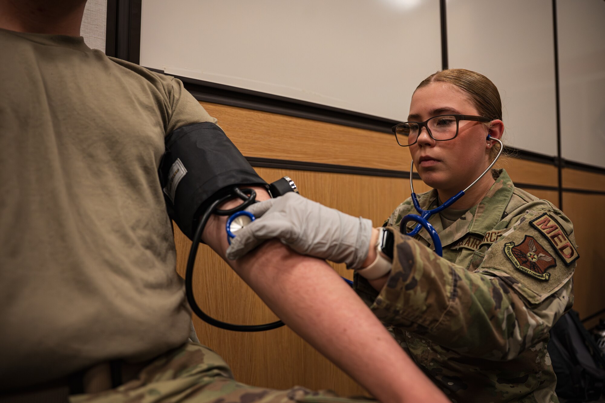 A uniformed woman conducts a blood pressure screening on a uniformed man.