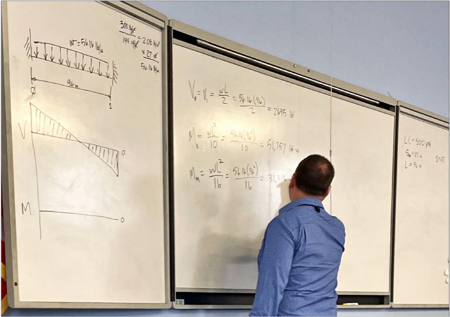 A man in a blue collard shirt writes mathematical equations on a whiteboard.