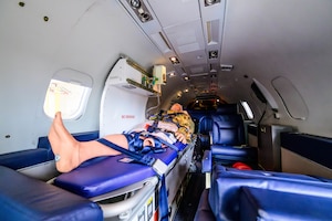 A medical dummy sits in a bed inside of a small jet. The dummy is surrounded by medical equipment.