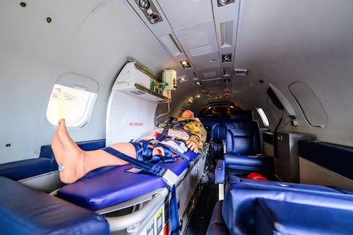 A medical dummy sits in a bed inside of a small jet. The dummy is surrounded by medical equipment.