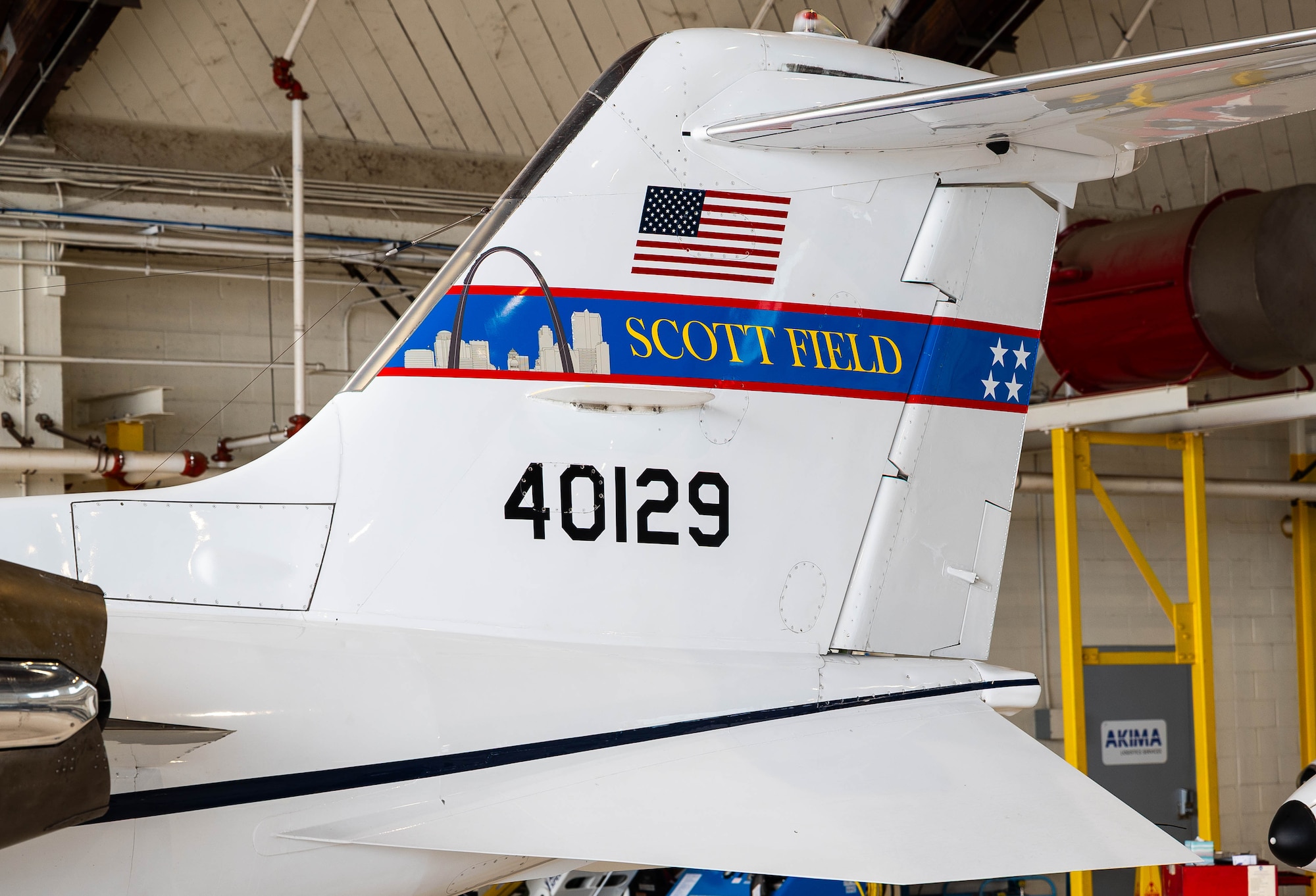 The tail of a C-21 is show. There is an American Flag with the words "Scott Field" under, and the numbers 40129 underneath as well.