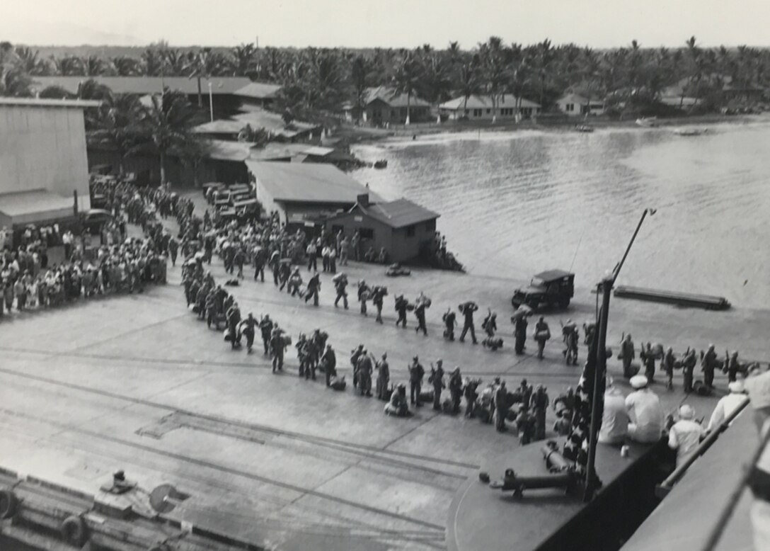 Black and white image of military members in a line boarding a ship.