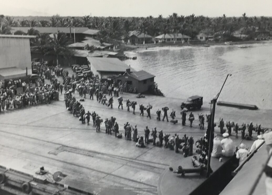 Black and white image of military members in a line boarding a ship.
